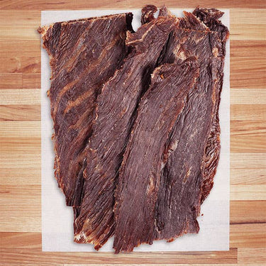 A wooden board with pieces of Farm Hounds Beef Jerky, showcasing the natural texture and thickness of the treat.