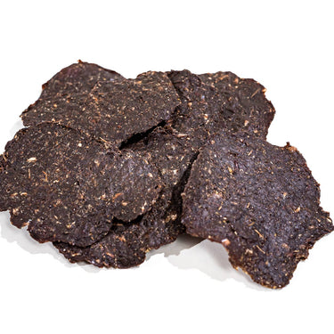 Elk jerky treats next to fresh rosemary, oregano, and sweet potatoes, emphasizing the organic, whole-food ingredients.